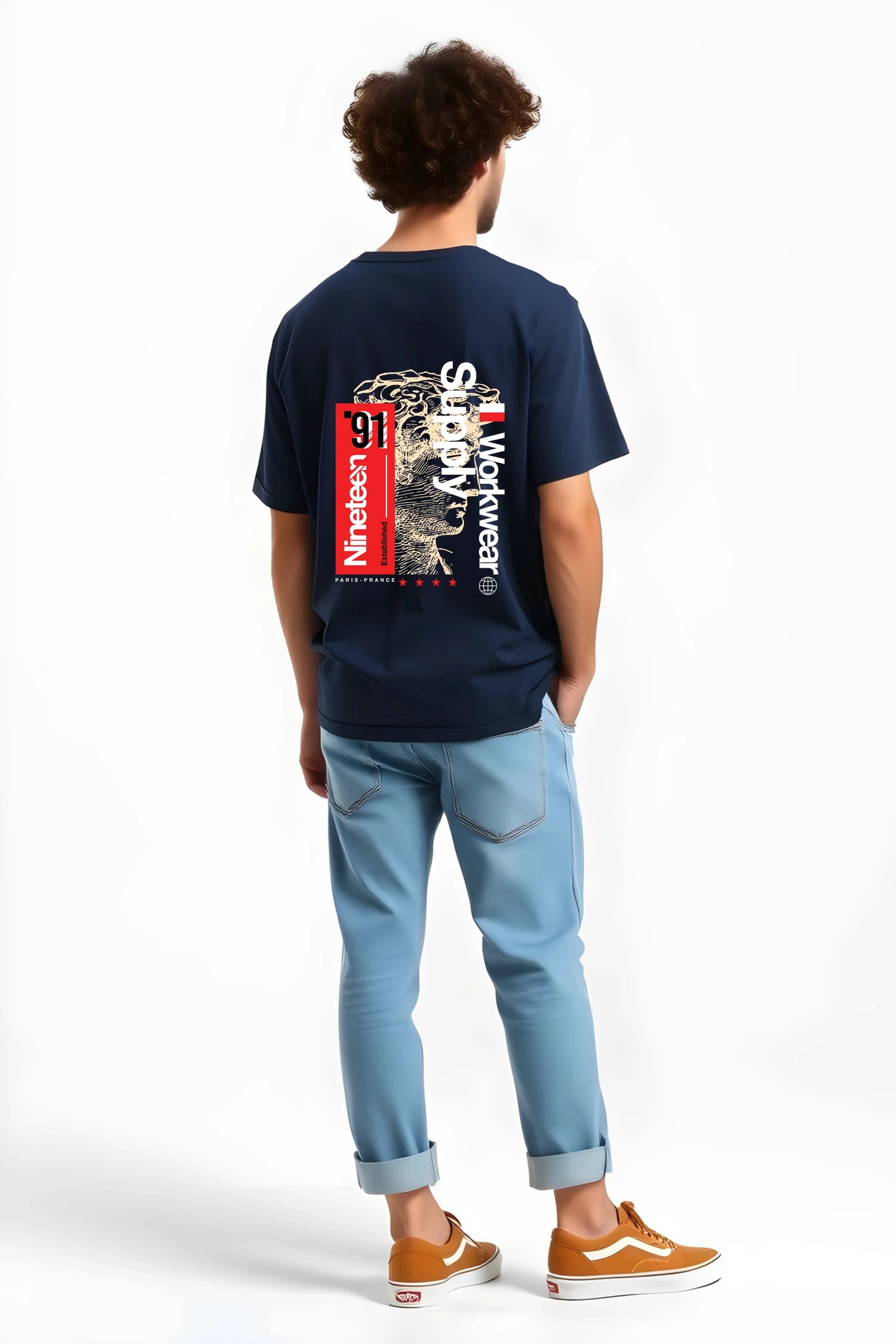 Back view of man wearing navy Nineteen ’91 Workwear Supply graphic t-shirt by Gill Harry, featuring bold red “Nineteen ’91” block and vintage-style face design, styled with light blue jeans and brown sneakers — minimalist streetwear with industrial edge