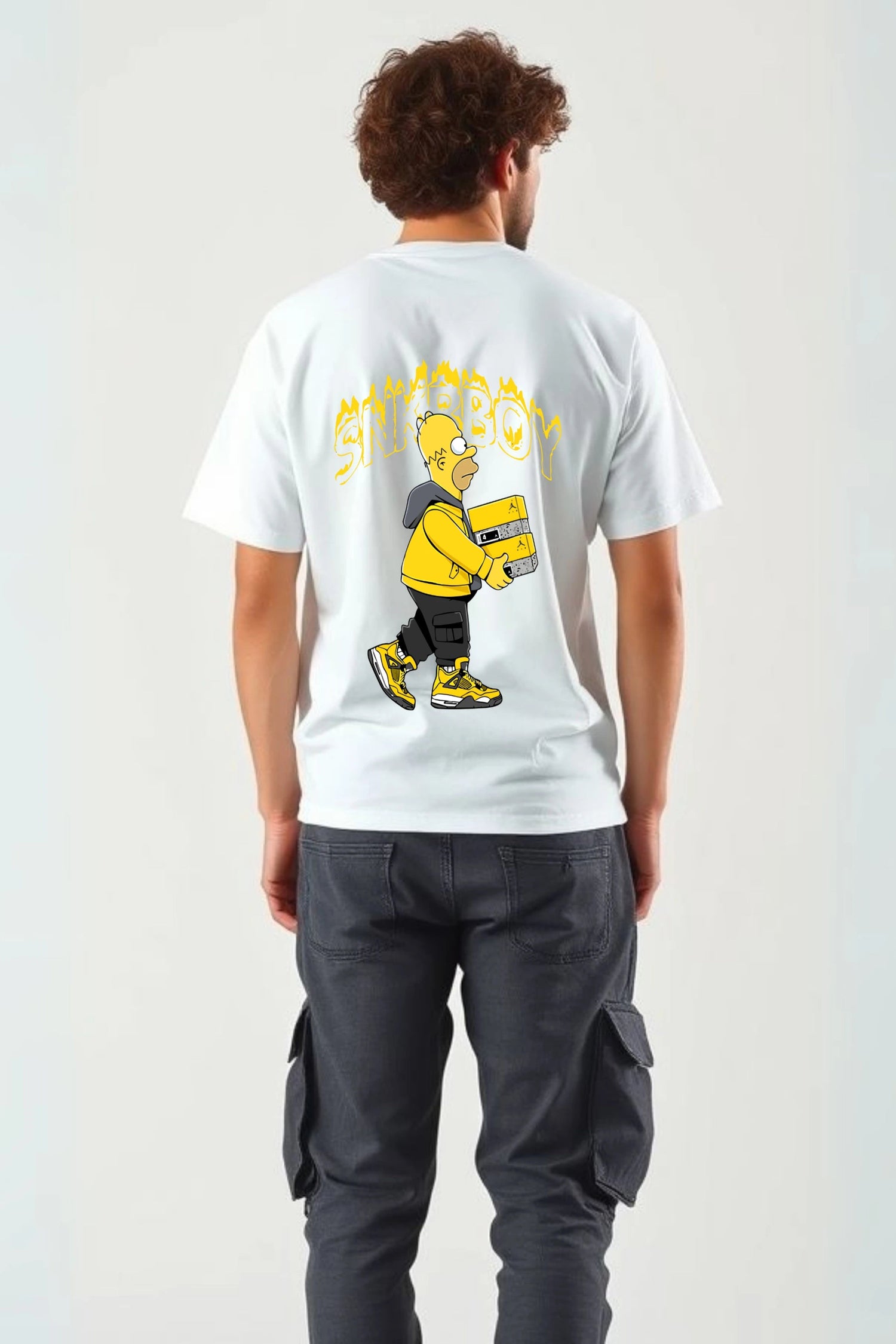 Back view of man wearing red SNKRBOY oversized graphic t-shirt by Gill Harry, featuring Homer Simpson as a sneakerhead holding a Jordan box, styled with dark cargo pants — bold streetwear for sneaker lovers and pop culture fans