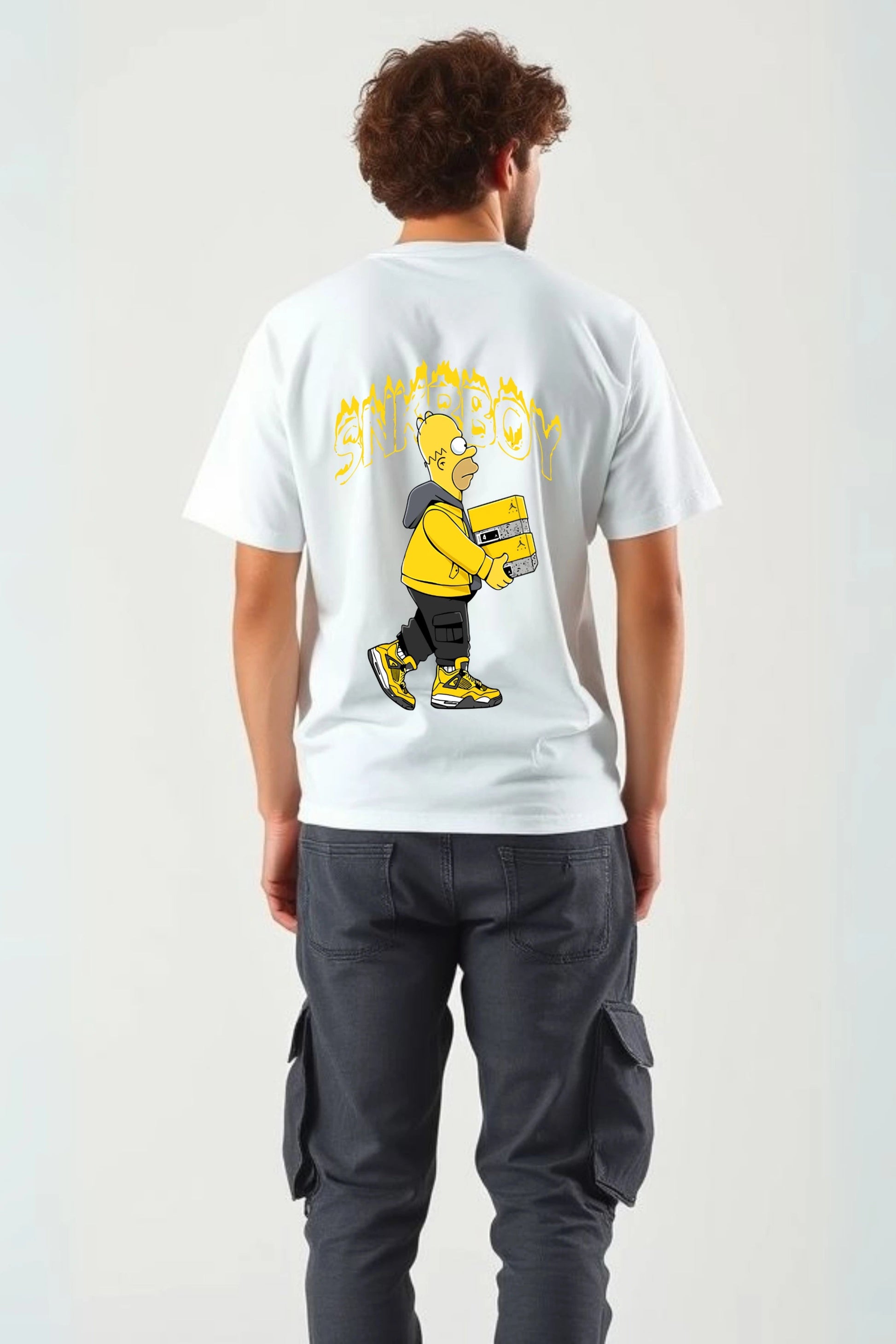 Back view of man wearing red SNKRBOY oversized graphic t-shirt by Gill Harry, featuring Homer Simpson as a sneakerhead holding a Jordan box, styled with dark cargo pants — bold streetwear for sneaker lovers and pop culture fans